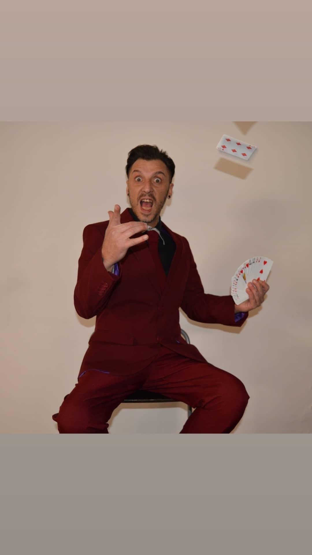 Massimo in abito rosso, con una carta sospesa sopra la mano.